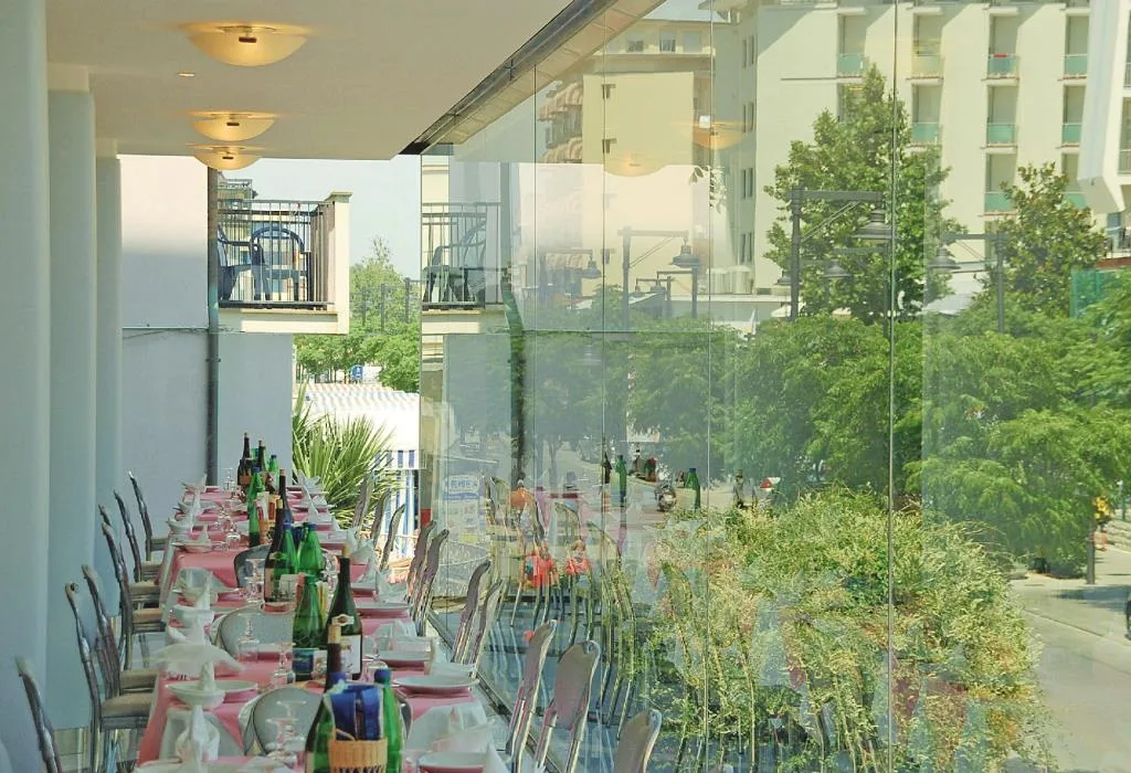 Veranda del ristorante con tavoli apparecchiati e vetrate affacciate sulla strada alberata