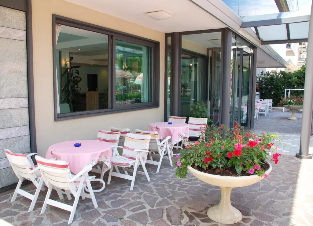 Terrazza esterna dell'hotel con tavolini rosa, sedie e fioriera con fiori colorati
