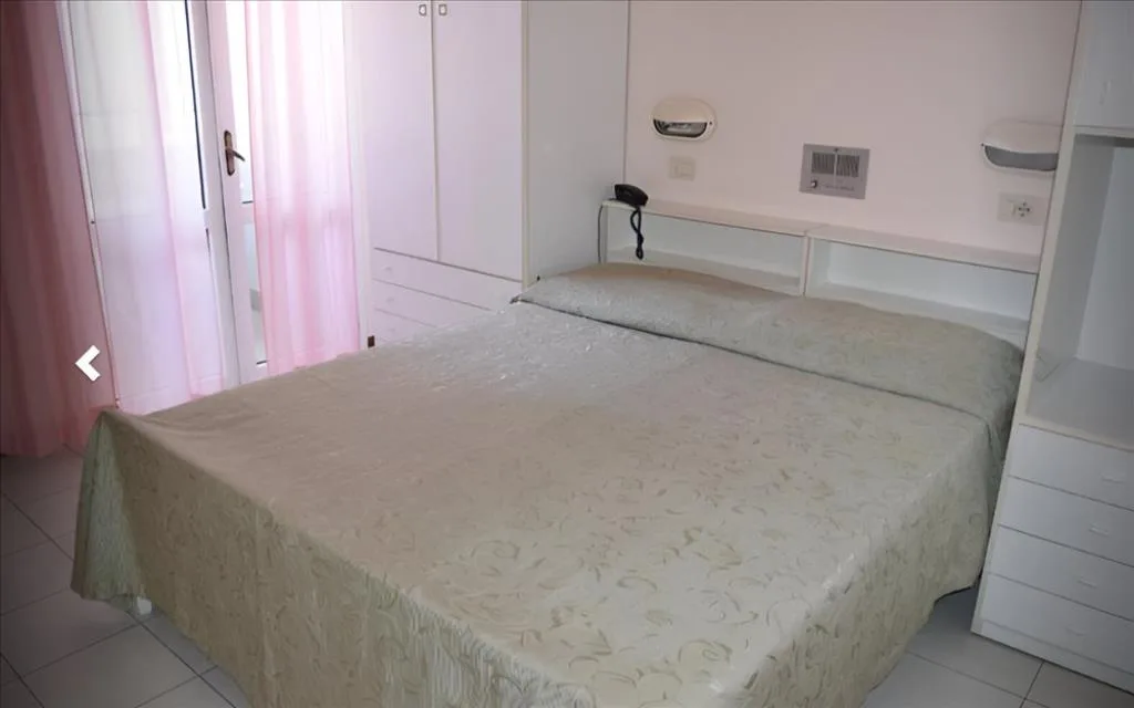 Camera doppia con letto matrimoniale, armadio bianco e tende rosa affacciate sul balcone