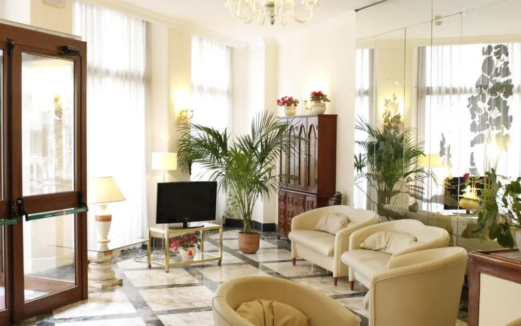 Hall dell'hotel con poltrone beige, pavimento in marmo, TV, piante e lampadario di vetro