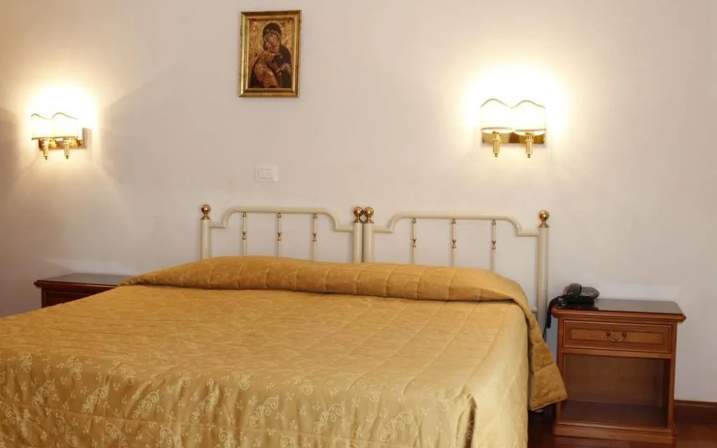 Letto matrimoniale con testiera in ferro battuto bianco, copriletto dorato, comodino in legno e quadro sacro