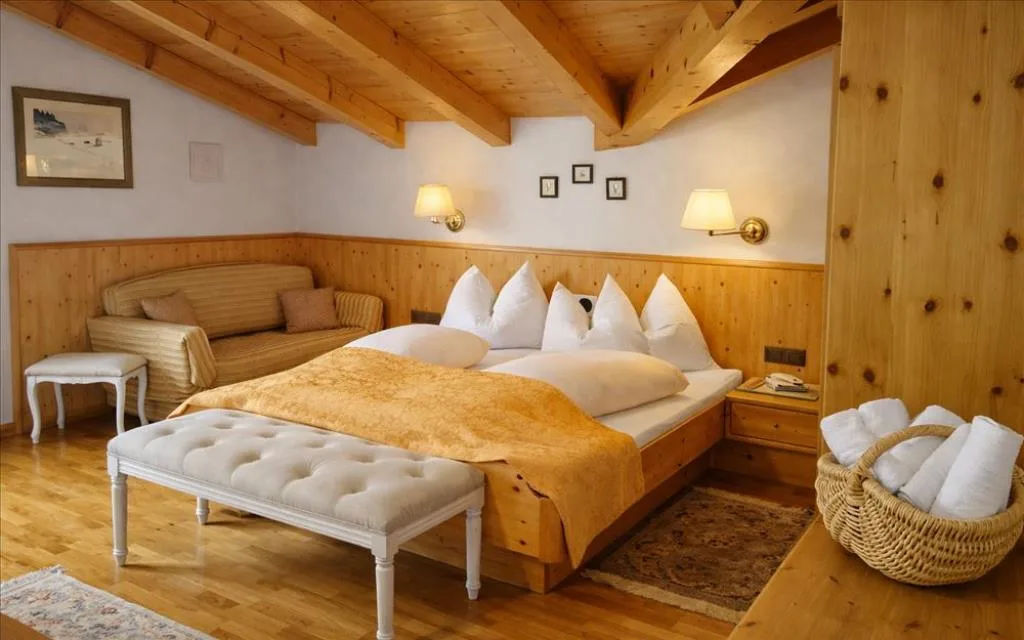 Camera mansardata con soffitto in legno, letto matrimoniale e divano in stile alpino