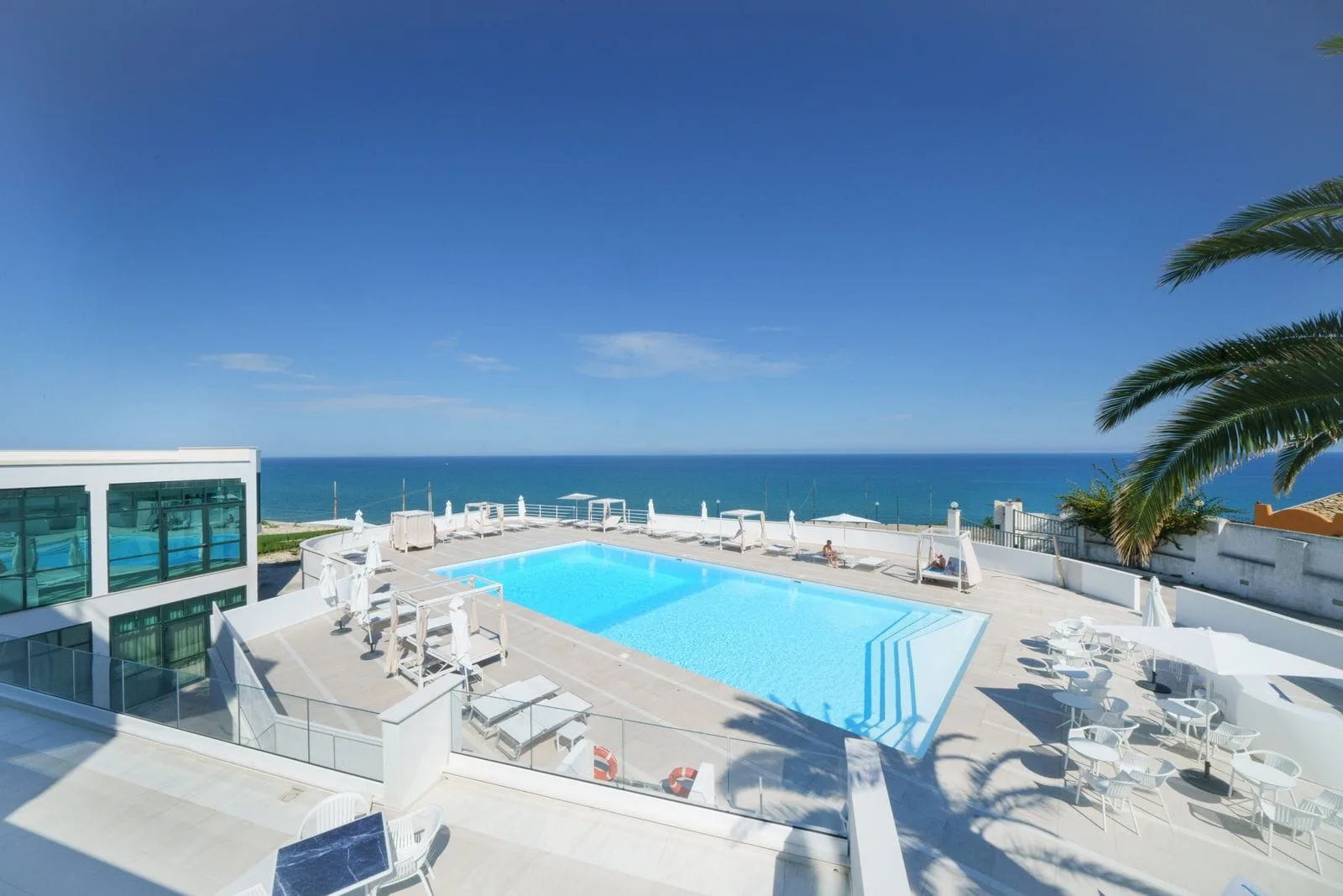 Terrazza con piscina, area lounge e panorama sul mare e palma