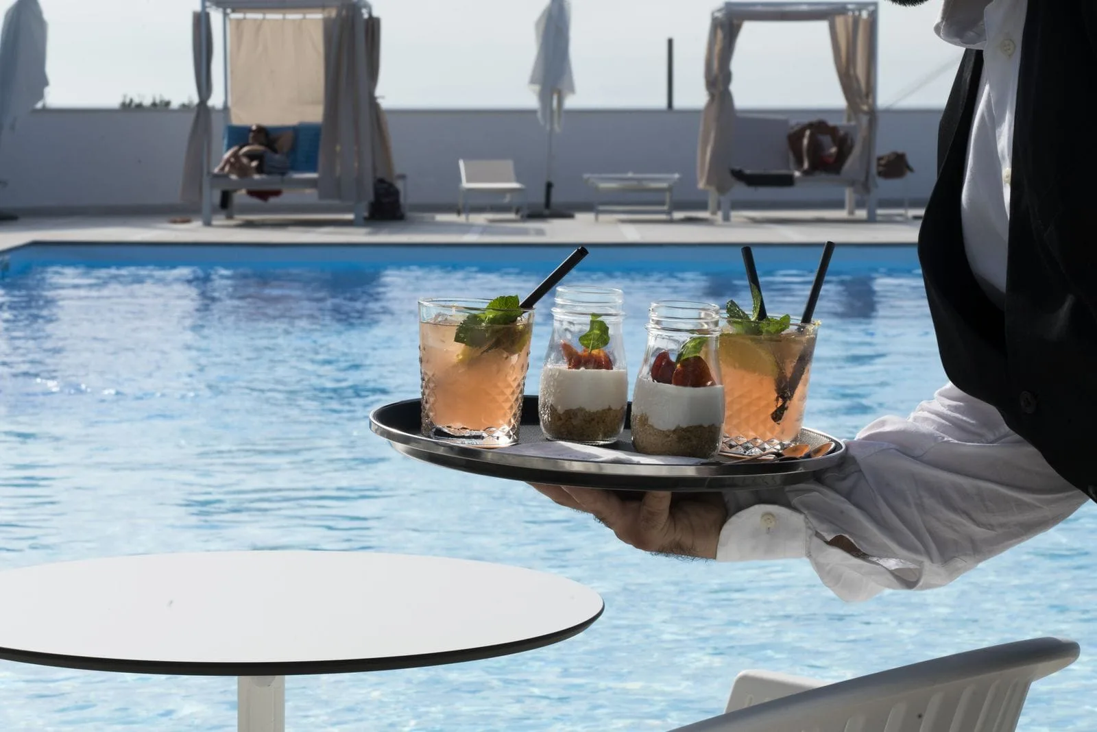 Cameriere serve cocktail e dessert su vassoio a bordo piscina