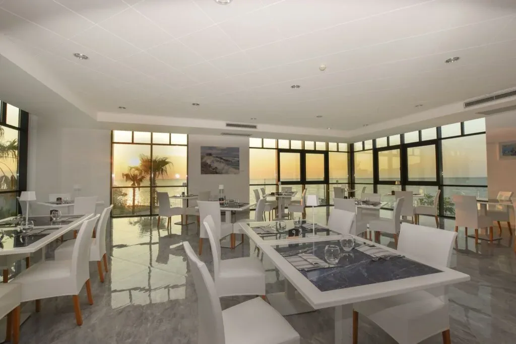 Sala ristorante elegante con tavoli apparecchiati e vista tramonto sul mare