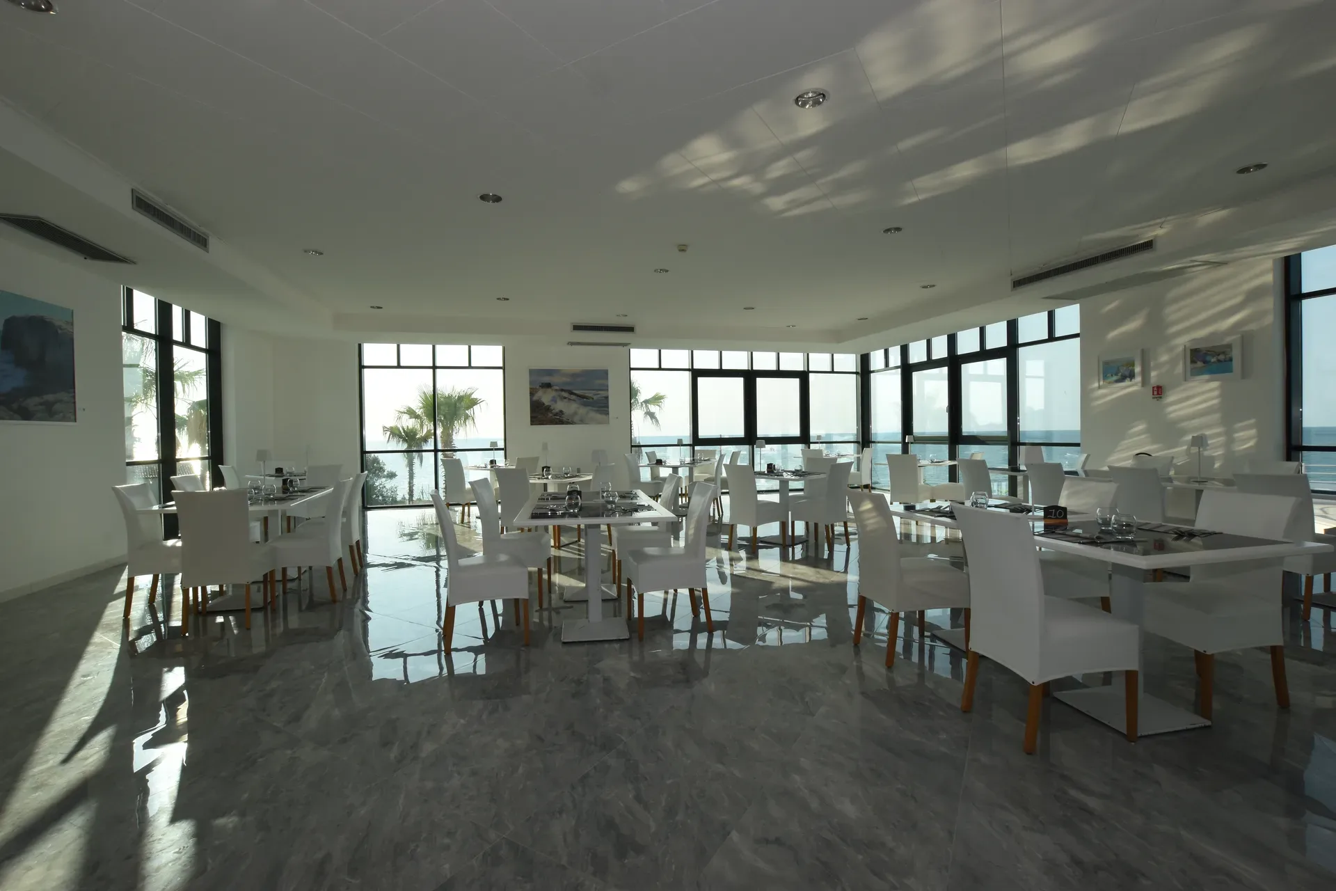 Ristorante interno con tavoli bianchi, pavimento lucido e vetrate panoramiche