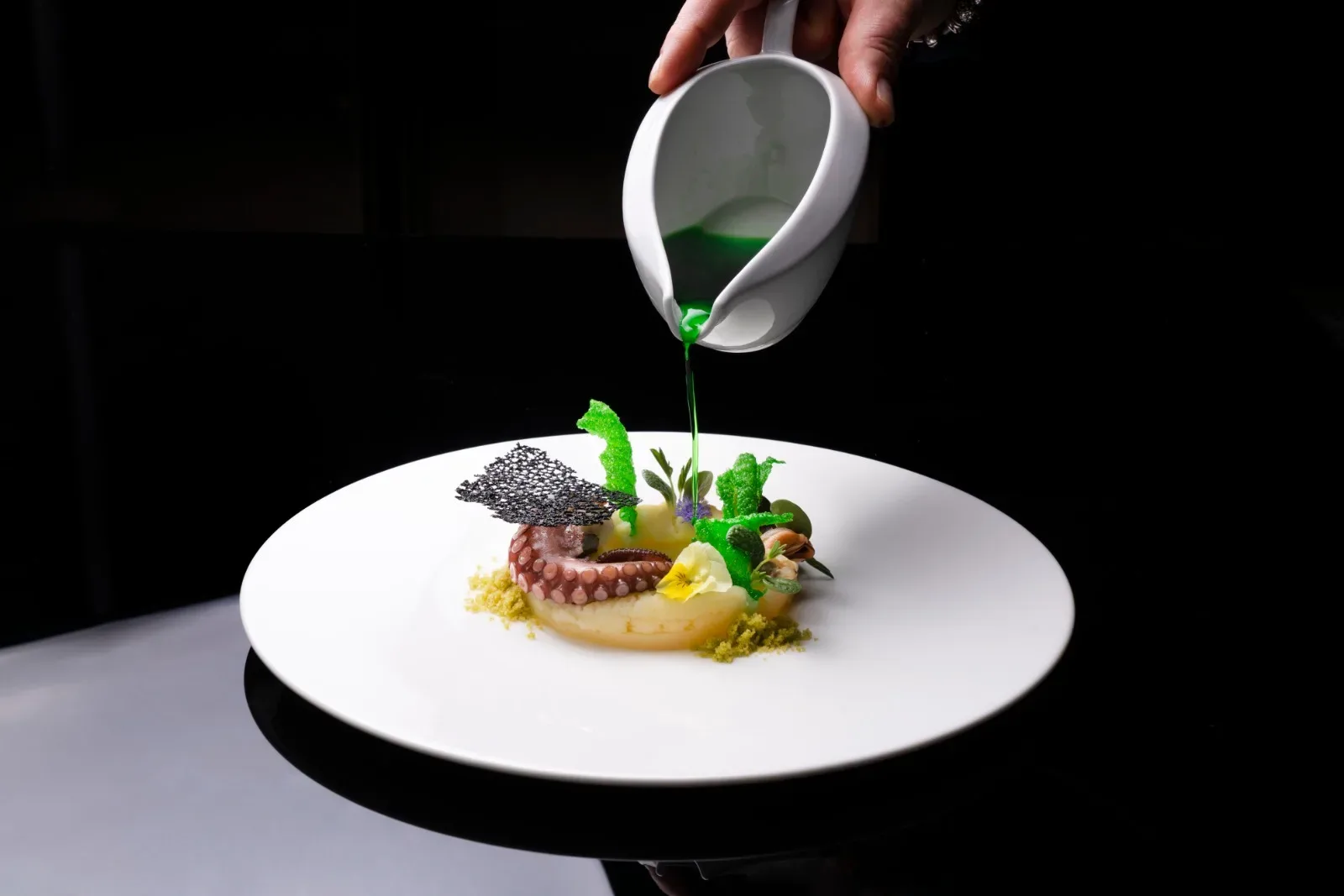 Impiattamento gourmet di polpo con salsa verde versata da brocca