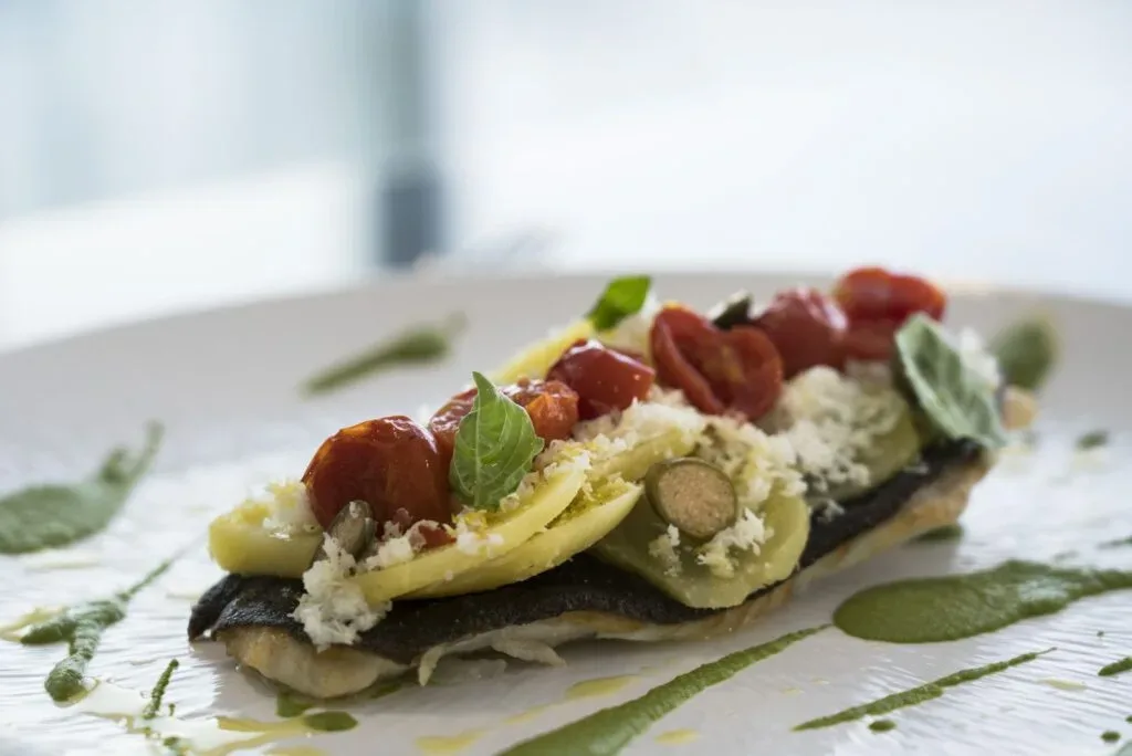 Piatto gourmet di pesce con pomodorini, basilico e verdure