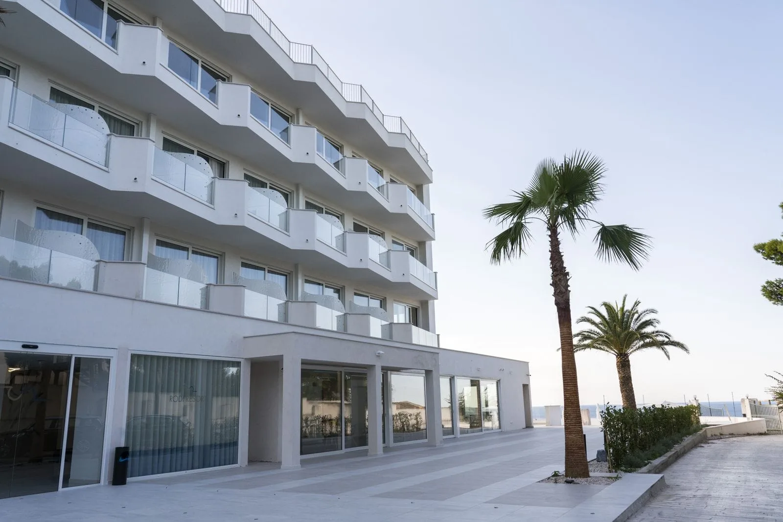 Esterno dell'hotel con balconi bianchi, ampia piazzola e palme