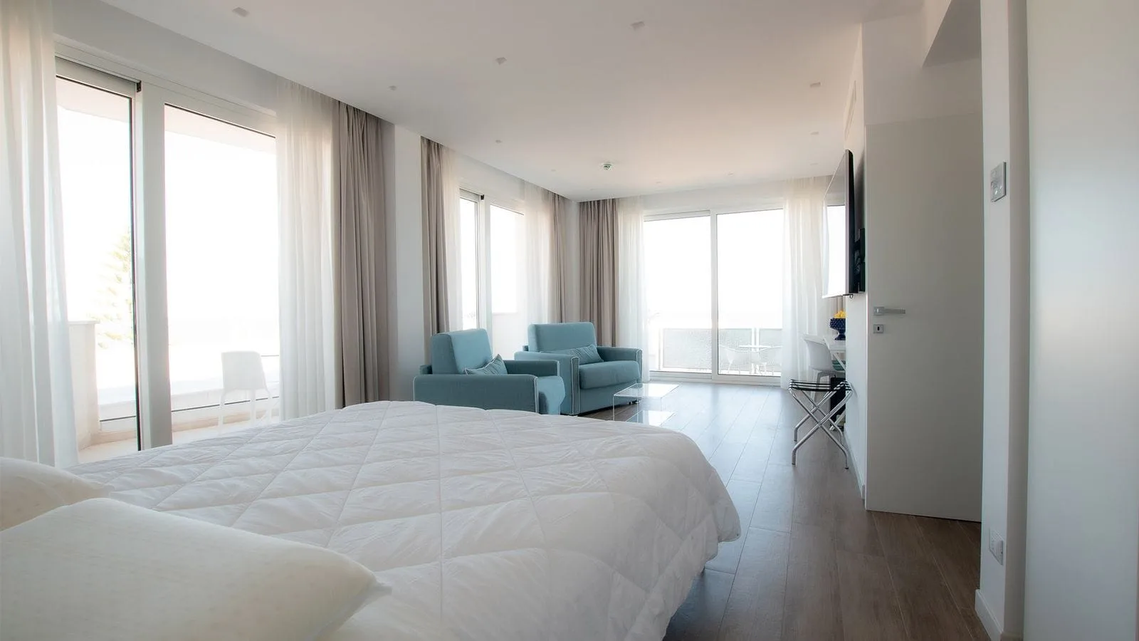 Ampia camera con letto matrimoniale, poltrone azzurre e grandi vetrate