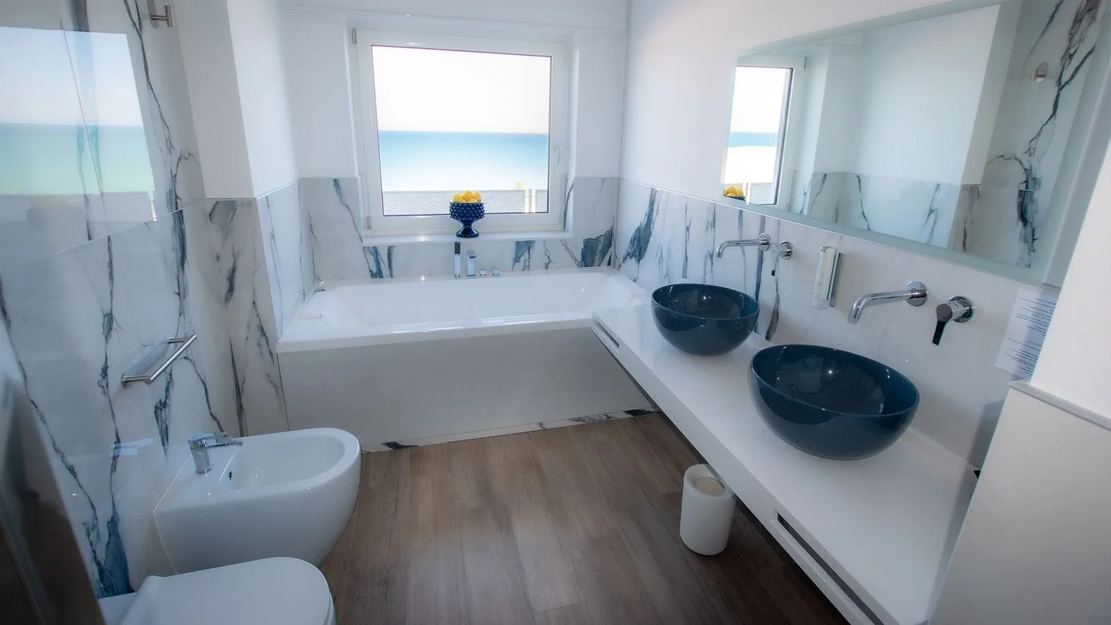 Bagno di lusso con vasca, doppio lavabo blu e finestra vista mare