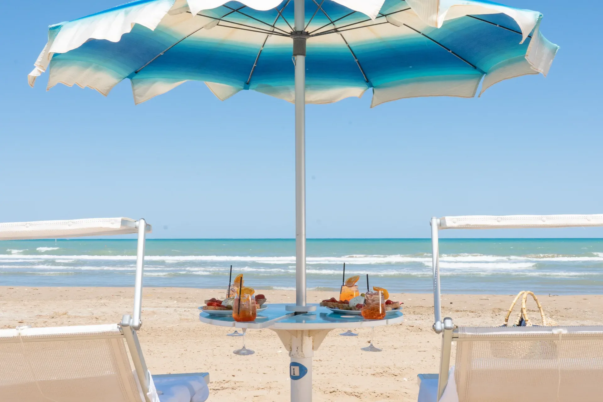 Ombrellone e lettini in spiaggia con aperitivo e vista sul mare