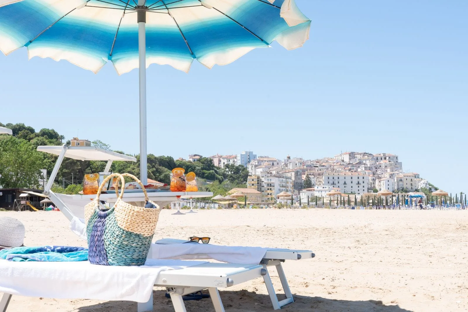 Spiaggia con lettino, ombrellone e vista sul borgo bianco arroccato