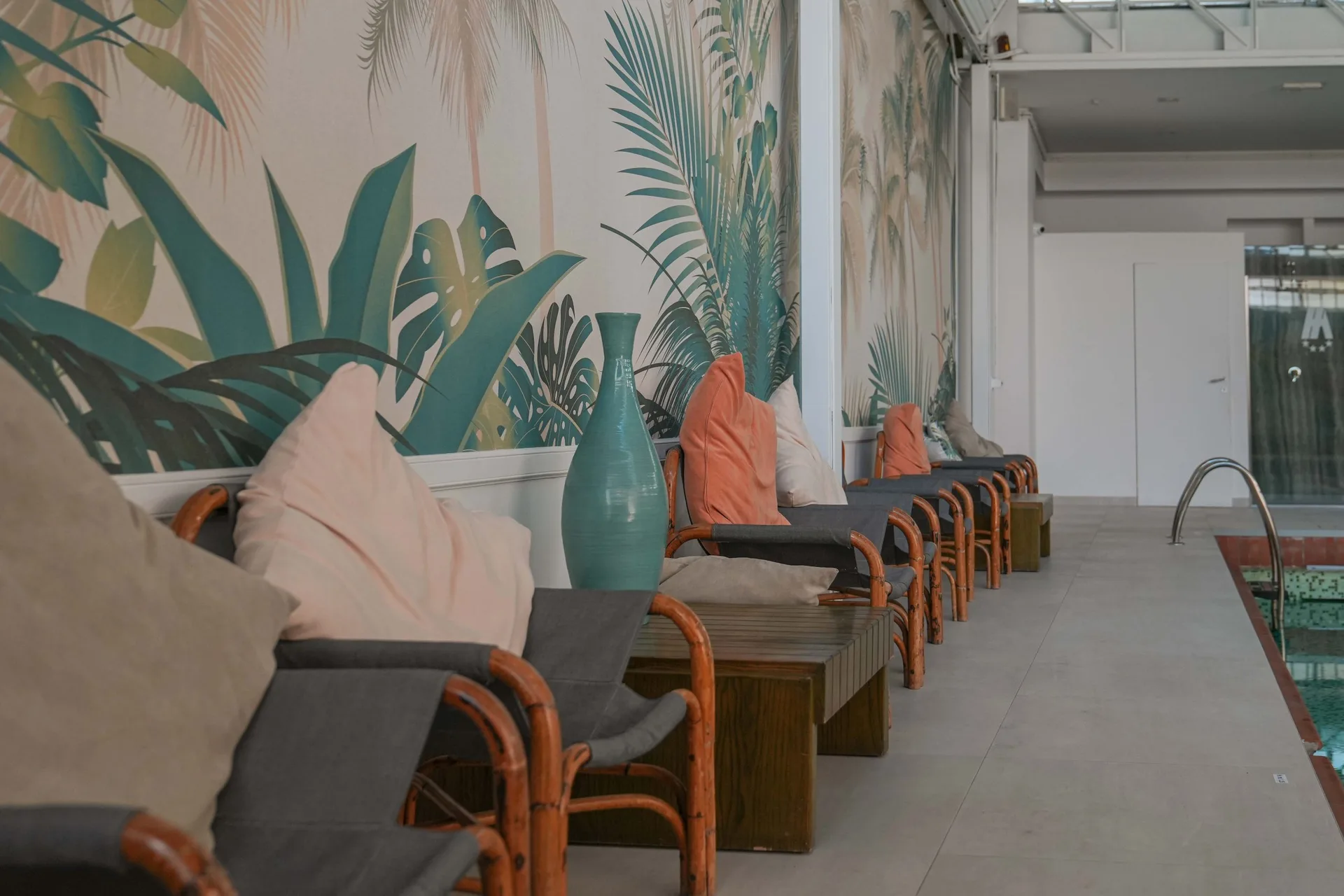 Poltrone in bambù con cuscini lungo la parete decorata con motivi tropicali vicino alla piscina