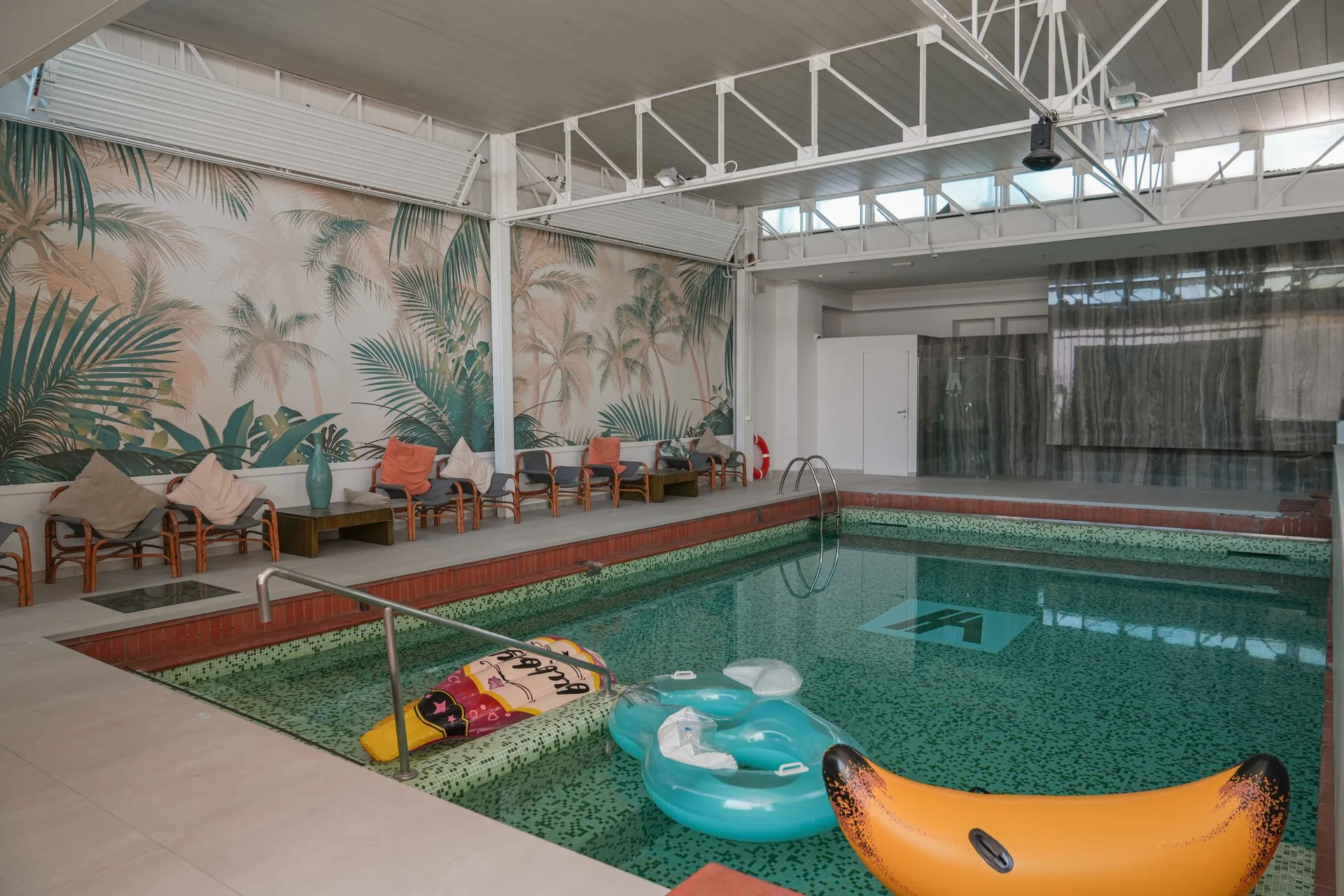 Piscina interna con murales tropicale e gonfiabili colorati galleggianti