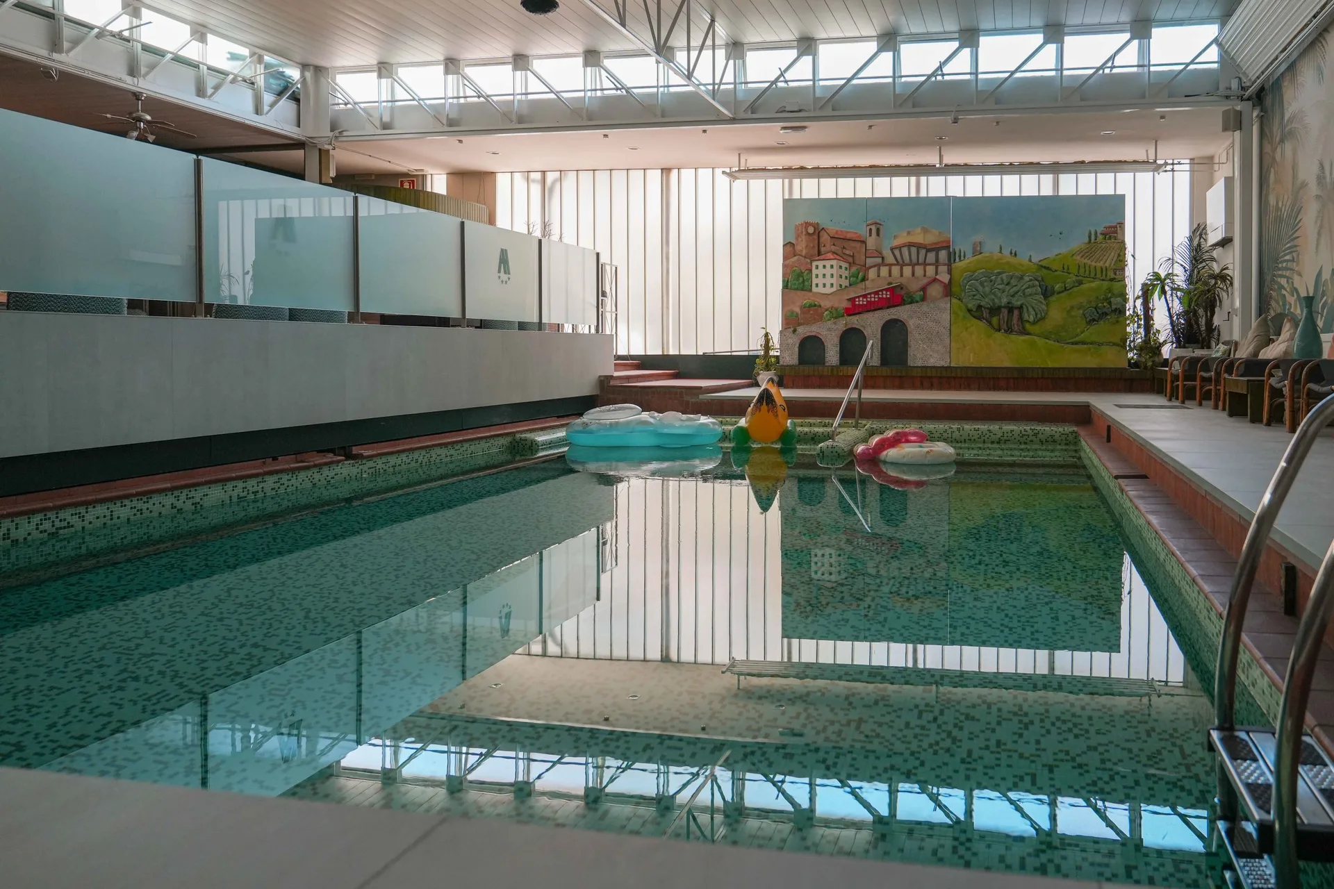 Piscina coperta con dipinto di paesaggio toscano e gonfiabili sull'acqua