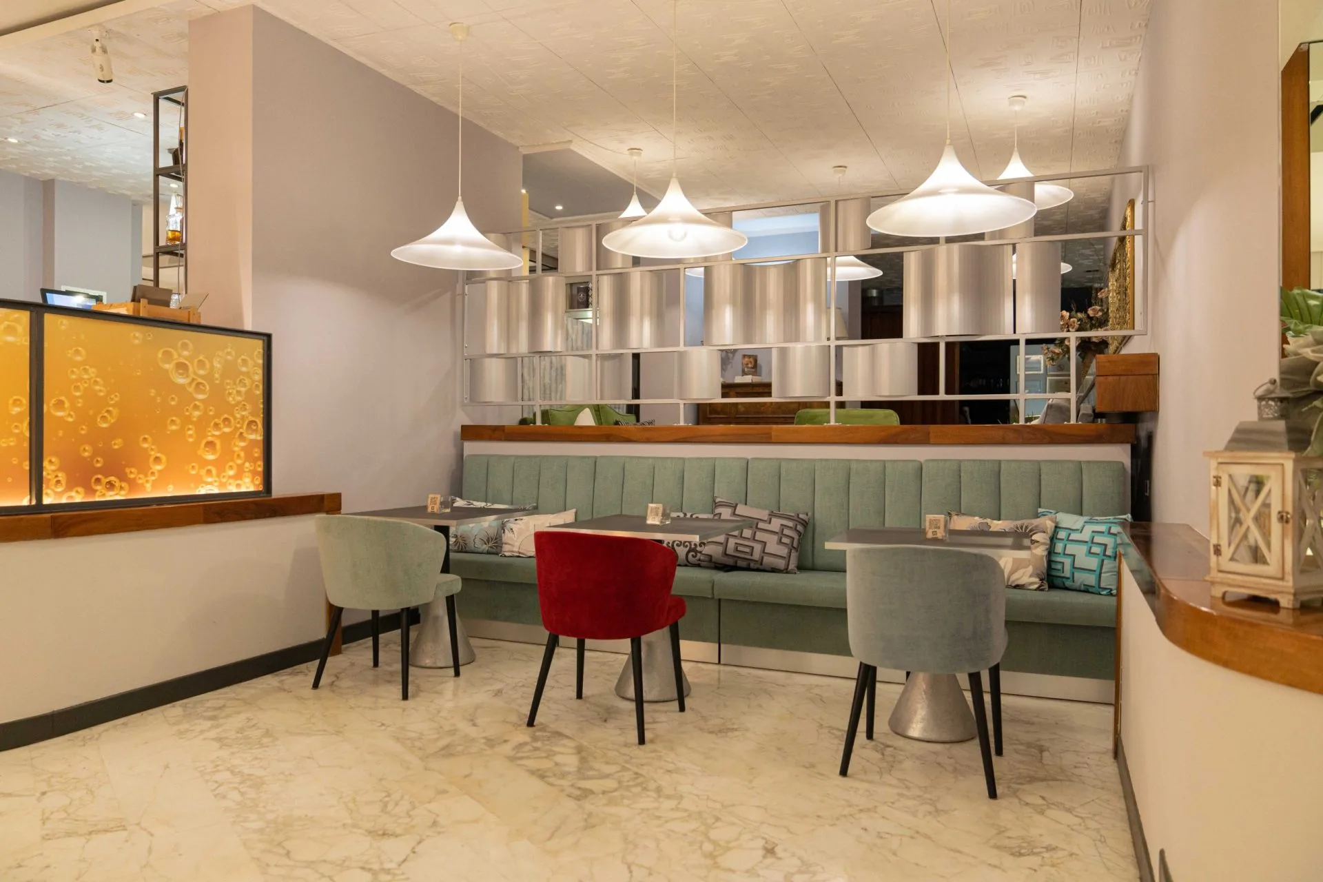 Sala bar dell'hotel con divano verde, sedie colorate e lampade a sospensione
