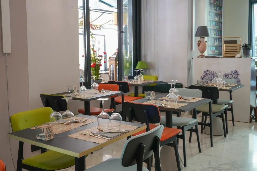 Sala ristorante luminosa con tavoli apparecchiati e sedie colorate