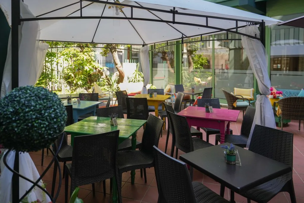 Dehors del ristorante con gazebo bianco, tavoli colorati e piante verdi