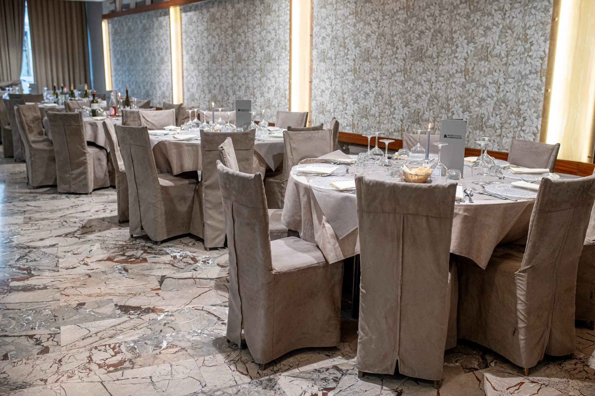Sala banchetti con tavoli rotondi apparecchiati e sedie foderate in velluto