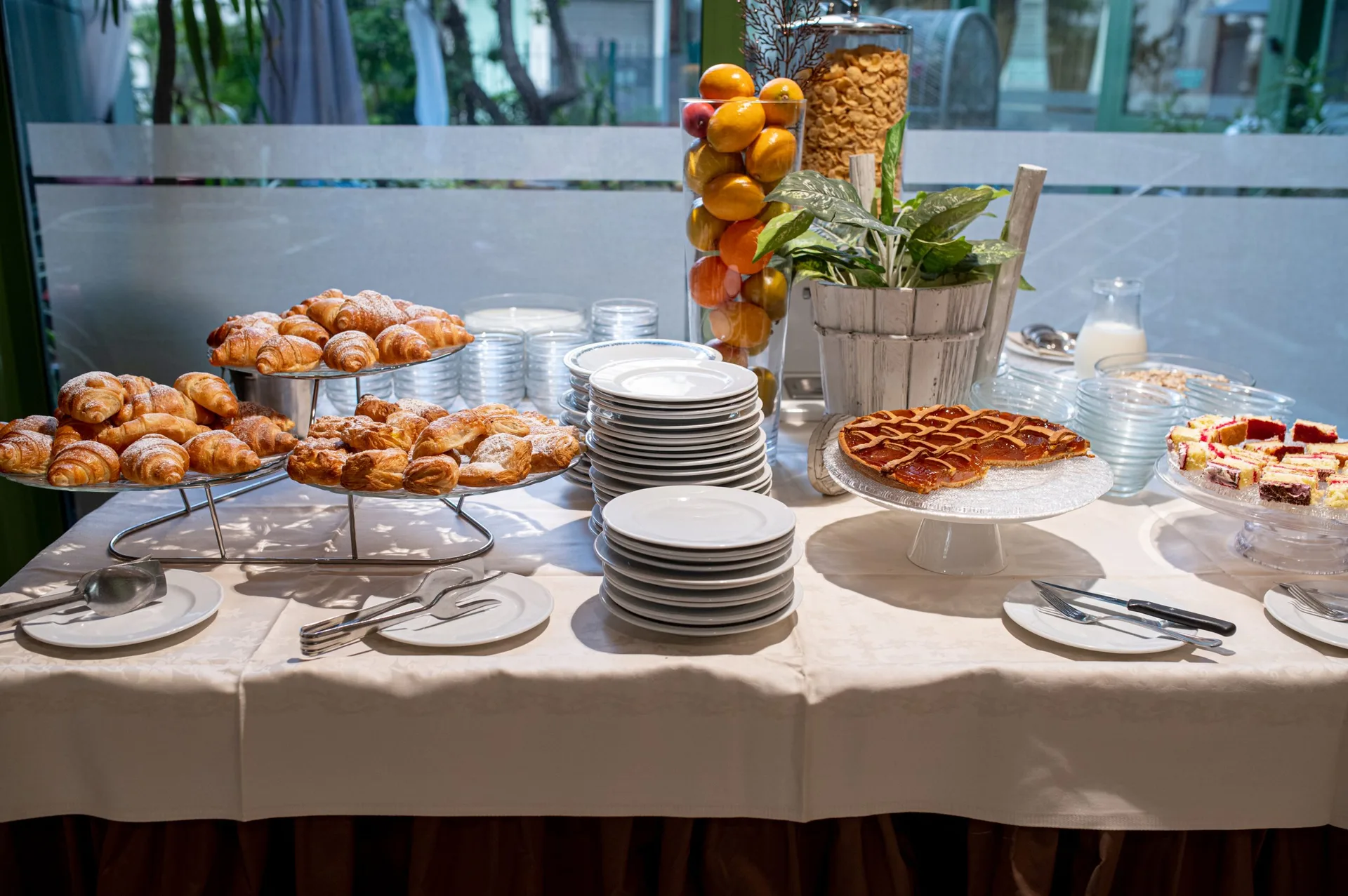 Tavolo della colazione con cornetti freschi, crostata e piatti impilati
