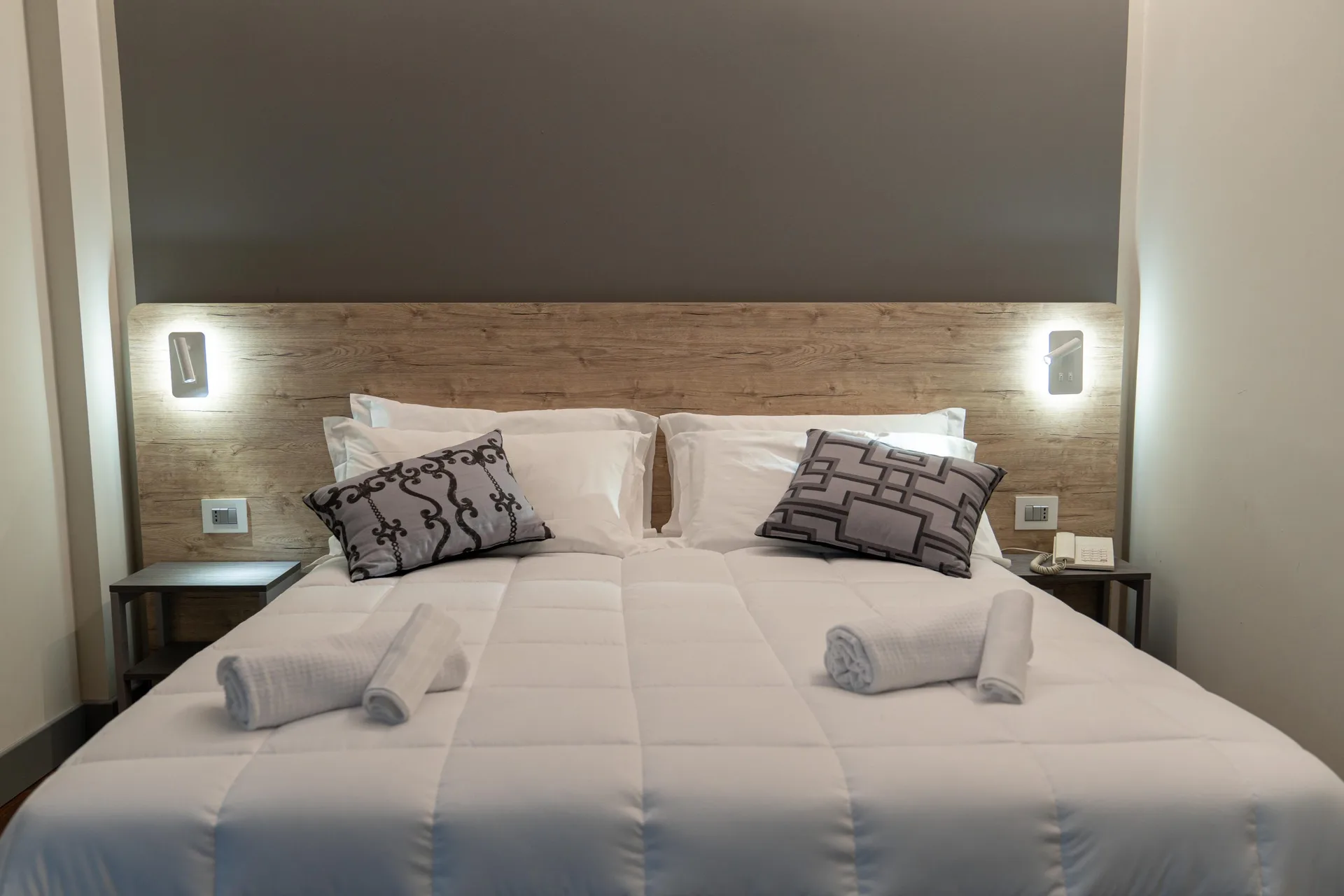 Letto matrimoniale con testiera in legno, cuscini decorativi e comodini
