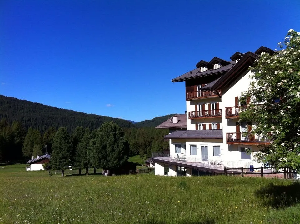 Esterno dell'hotel con balconi in legno circondato da prati verdi e cielo azzurro