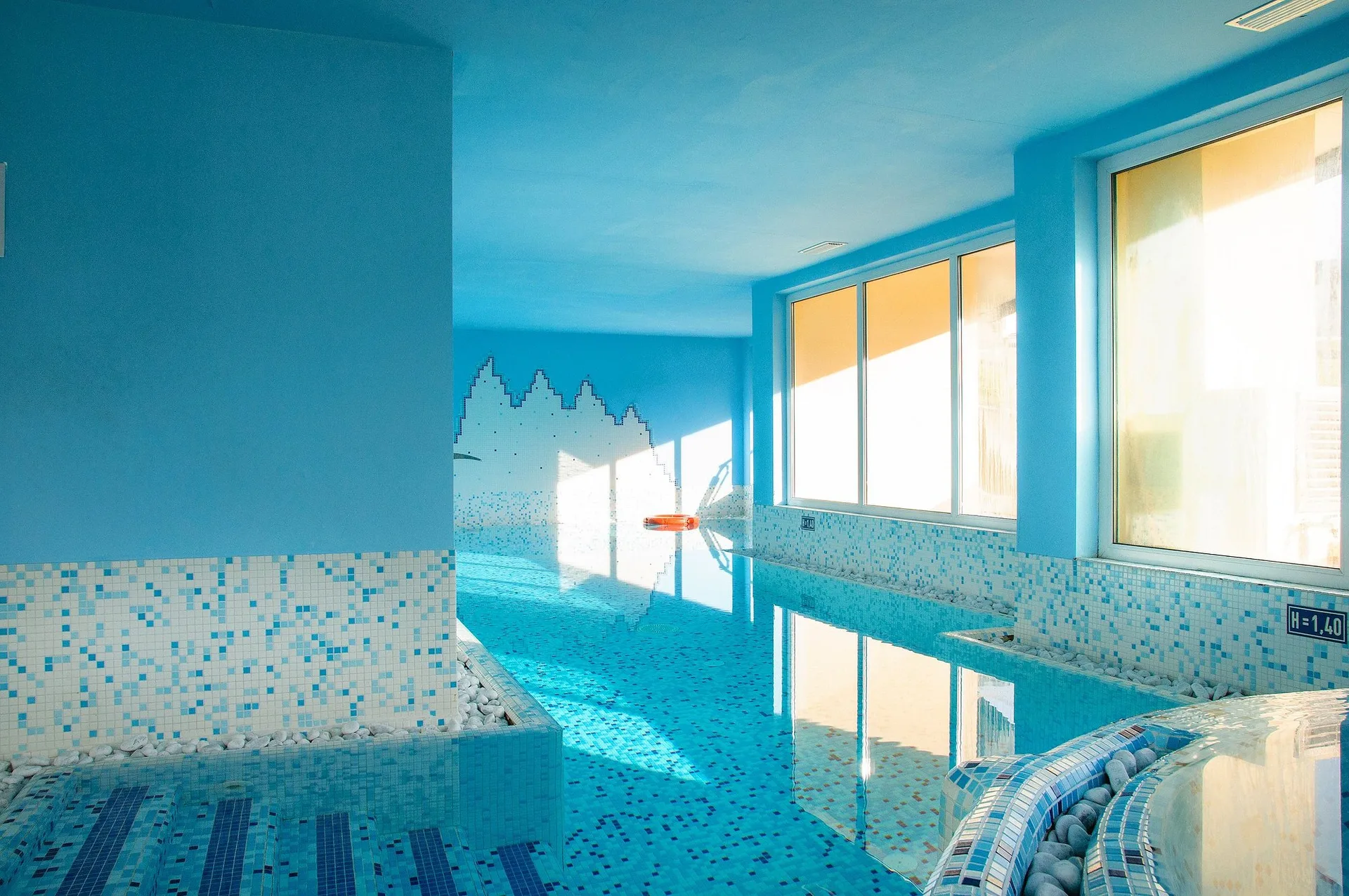 Piscina interna con acqua azzurra, mosaici e ampie finestre luminose