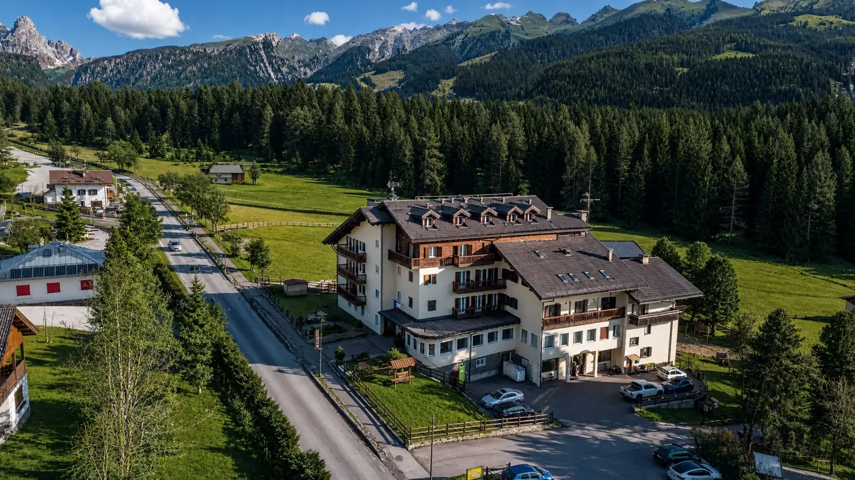 Vista aerea dell'hotel lungo la strada con boschi e Dolomiti sullo sfondo