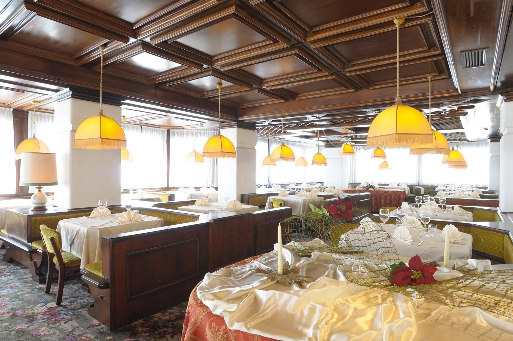 Ampia sala da pranzo con soffitto a cassettoni in legno e tavoli riccamente apparecchiati