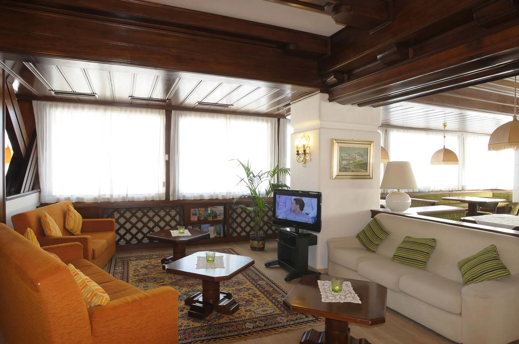 Salotto dell'hotel con divani, poltrone arancioni, TV e soffitto in legno scuro