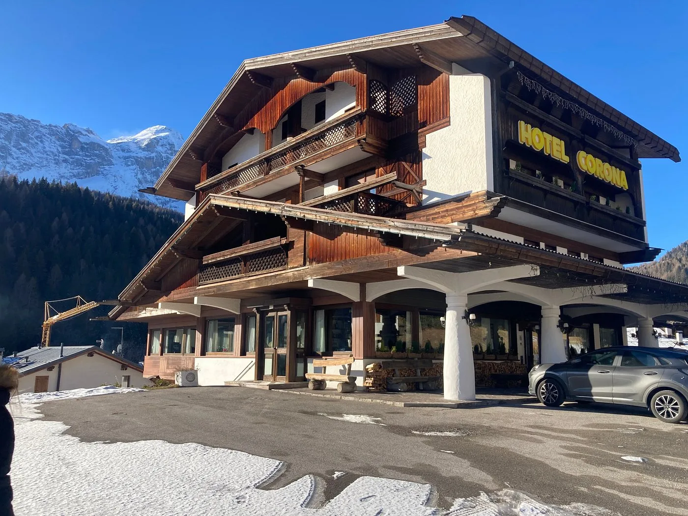 Facciata dell'Hotel Corona in stile chalet con portico e montagne innevate sullo sfondo