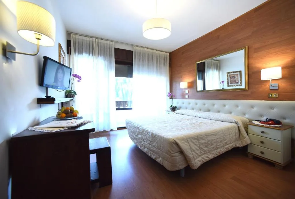 Camera matrimoniale moderna con testiera imbottita, TV e parete in legno