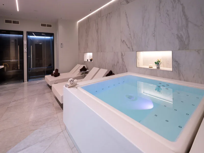 Zona spa con vasca idromassaggio, lettini relax e pareti in marmo