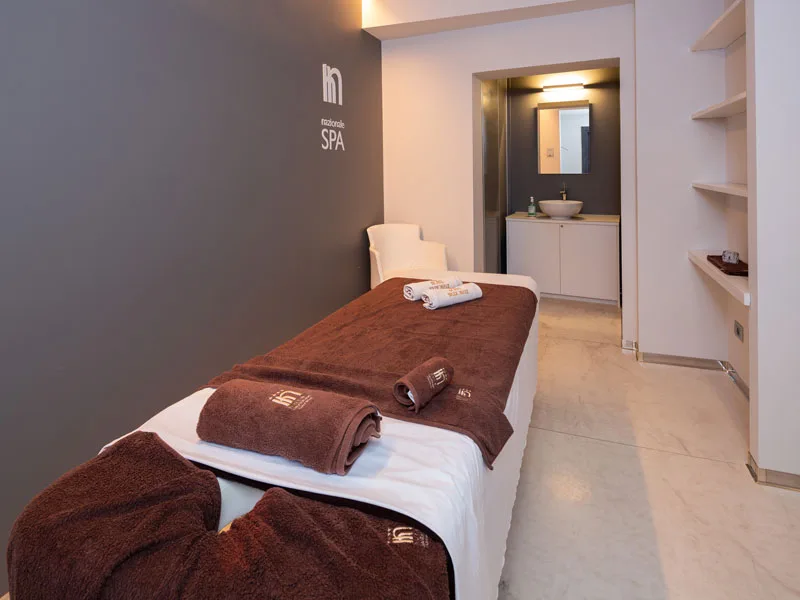 Cabina massaggi della spa con lettino, asciugamani marroni e bagno privato