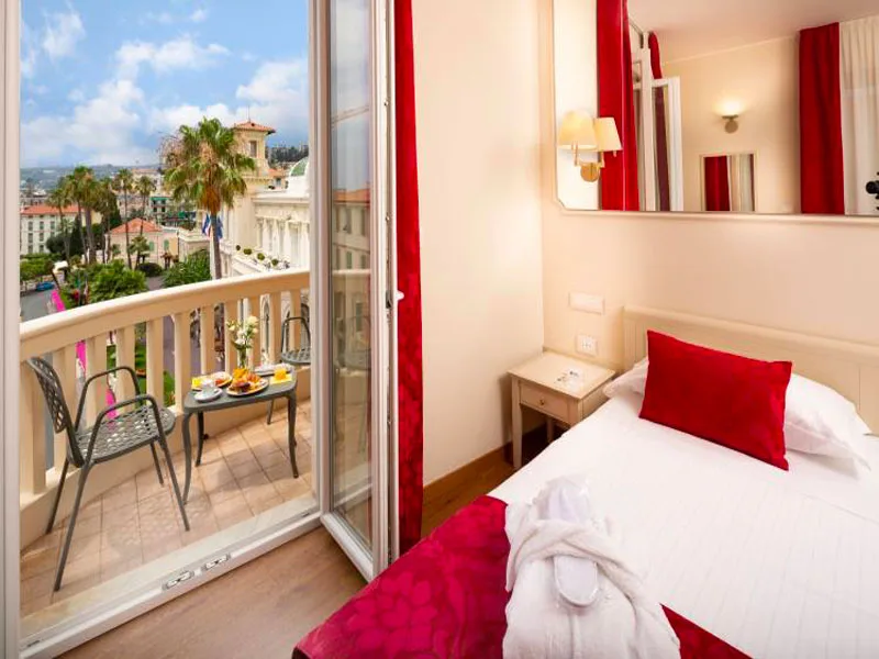 Camera con balcone vista città, letto con cuscino rosso e vassoio colazione all'esterno