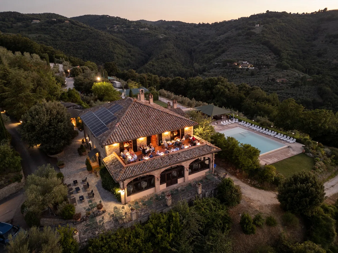 Casale illuminato all'imbrunire con terrazza ristorante e piscina tra le colline