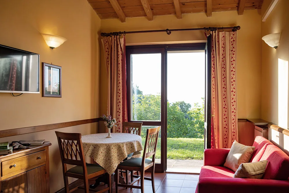 Soggiorno di appartamento con divano rosso, tavolo da pranzo e porta sul giardino
