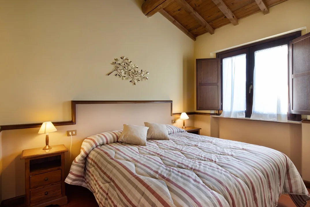 Camera matrimoniale con testiera imbottita, copriletto a righe e travi in legno