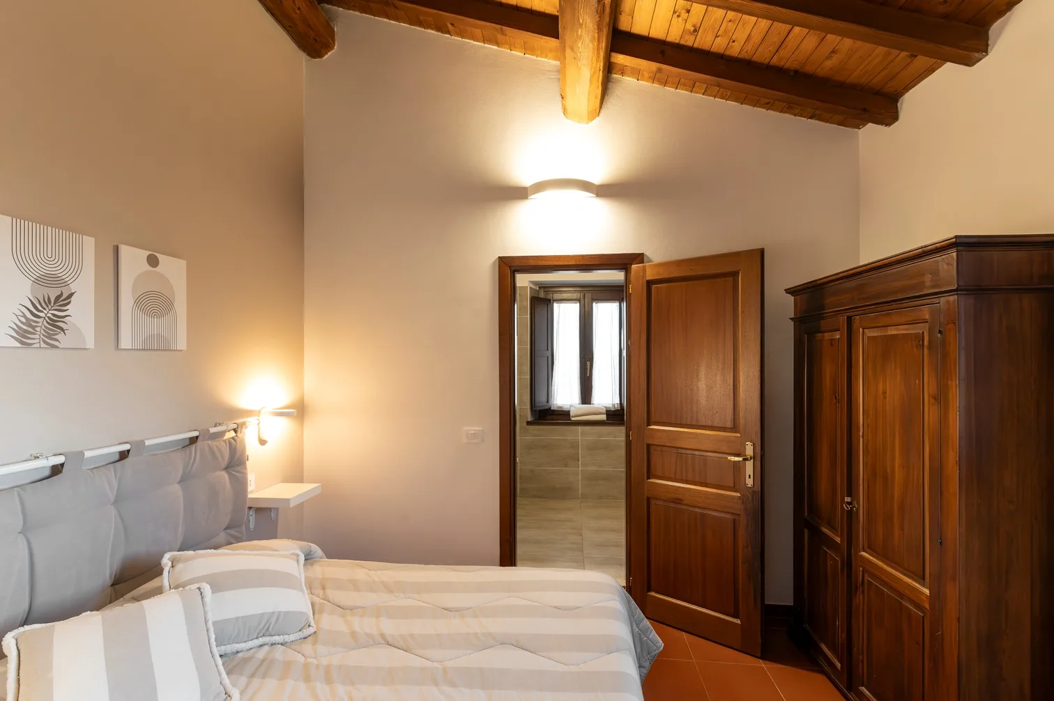 Camera moderna con testiera grigia, armadio in legno e bagno privato adiacente