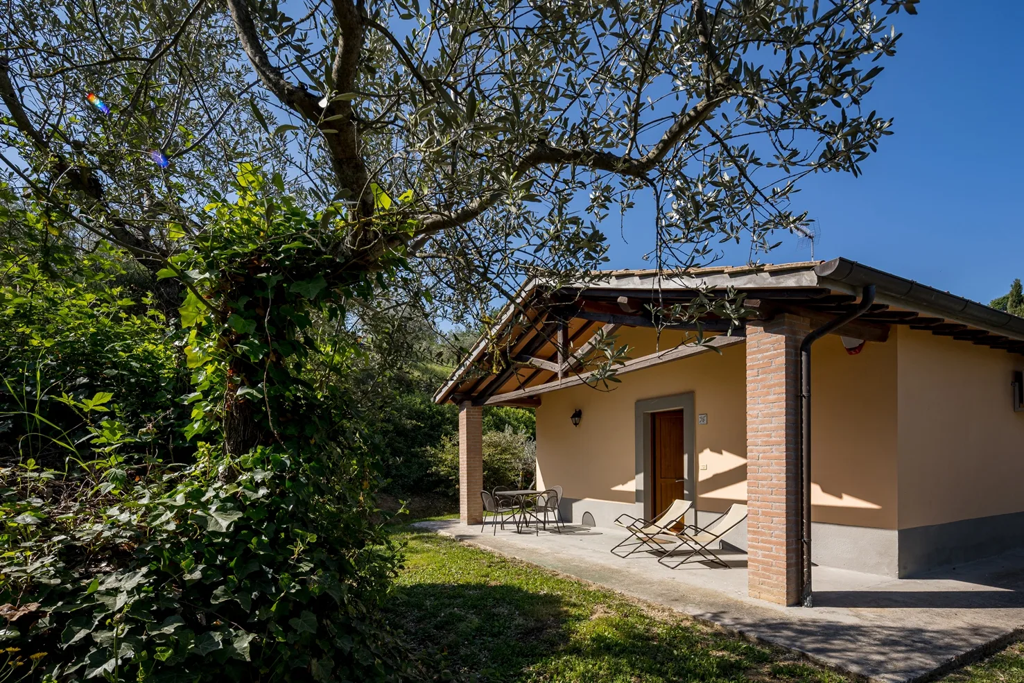 Casetta in stile toscano con portico in mattoni, tavolo e sdraio in giardino