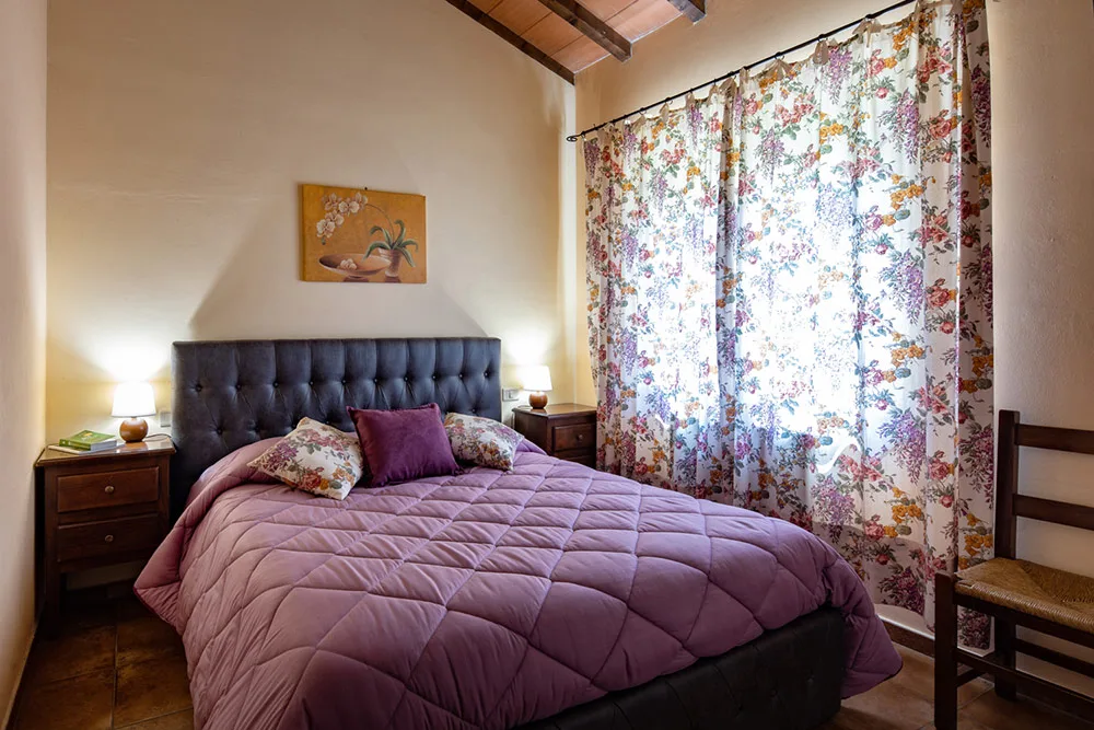 Camera da letto con testiera imbottita scura, copriletto viola e tende floreali