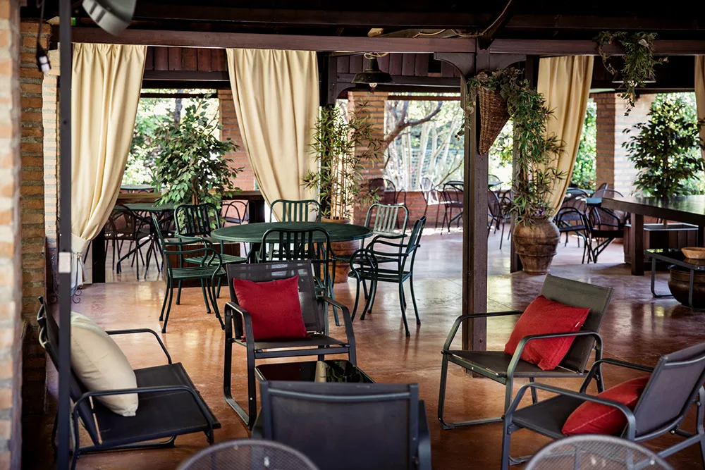 Area lounge coperta con poltrone, cuscini rossi e tavoli in ferro dallo stile rustico