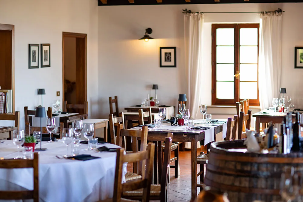 Sala ristorante interna con tavoli in legno apparecchiati, luce naturale e arredo rustico