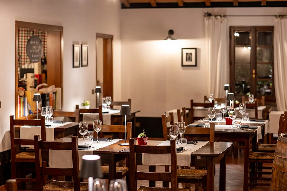 Sala da pranzo interna in stile rustico con tavoli in legno, lampade e botte in legno