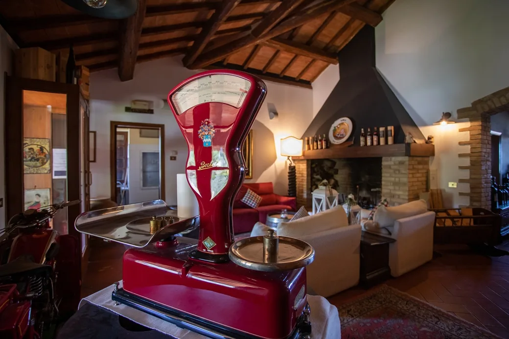 Salotto rustico con bilancia rossa d'epoca, camino in mattoni e divani accoglienti