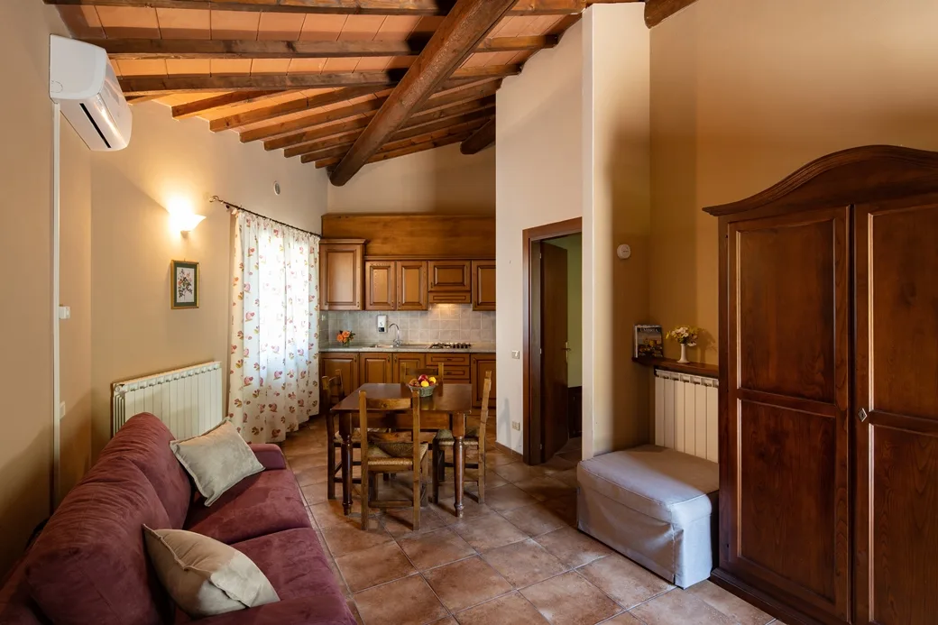 Soggiorno con angolo cottura in legno, divano, soffitto in travi e climatizzatore