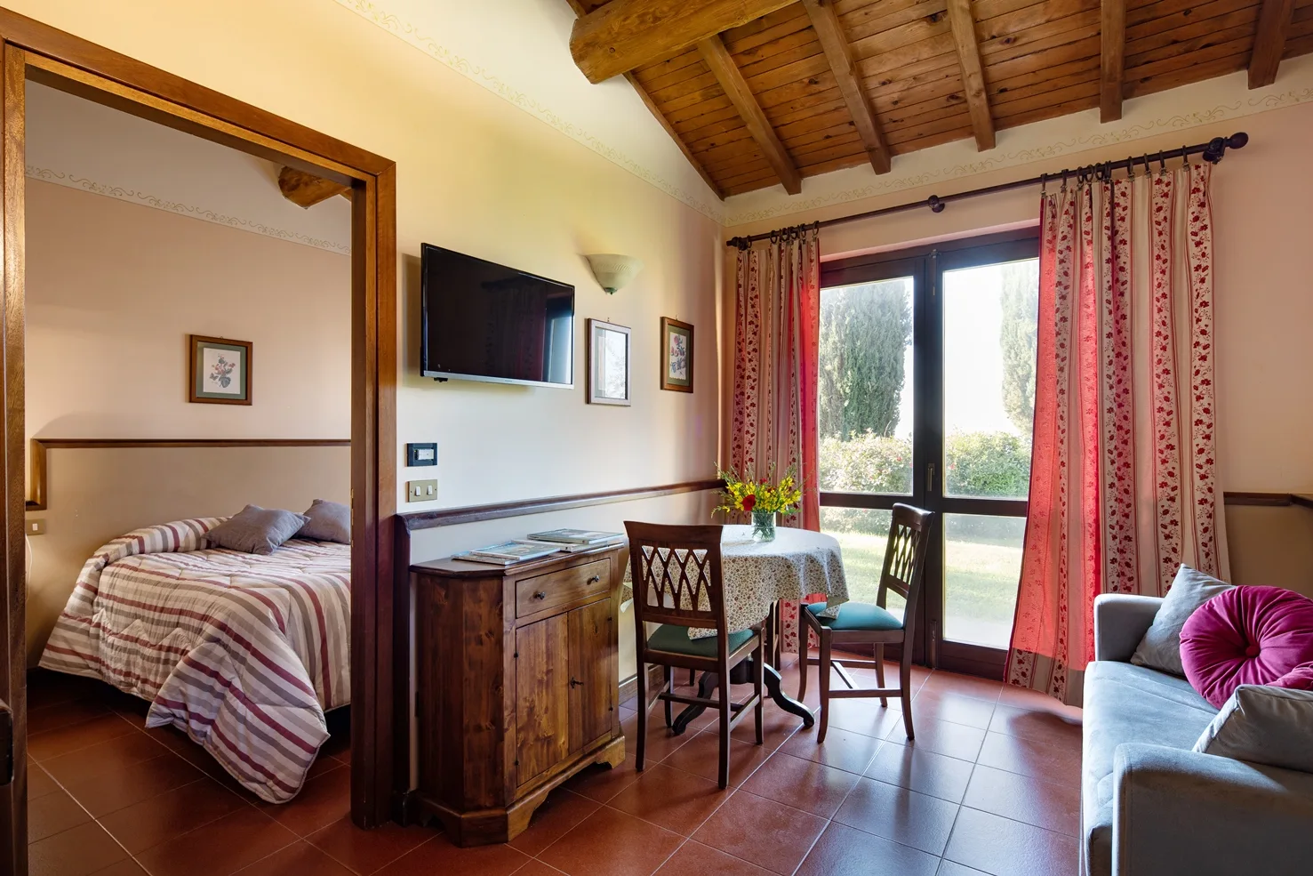 Camera con angolo salotto, TV, tavolino e vista sul giardino attraverso ampia finestra