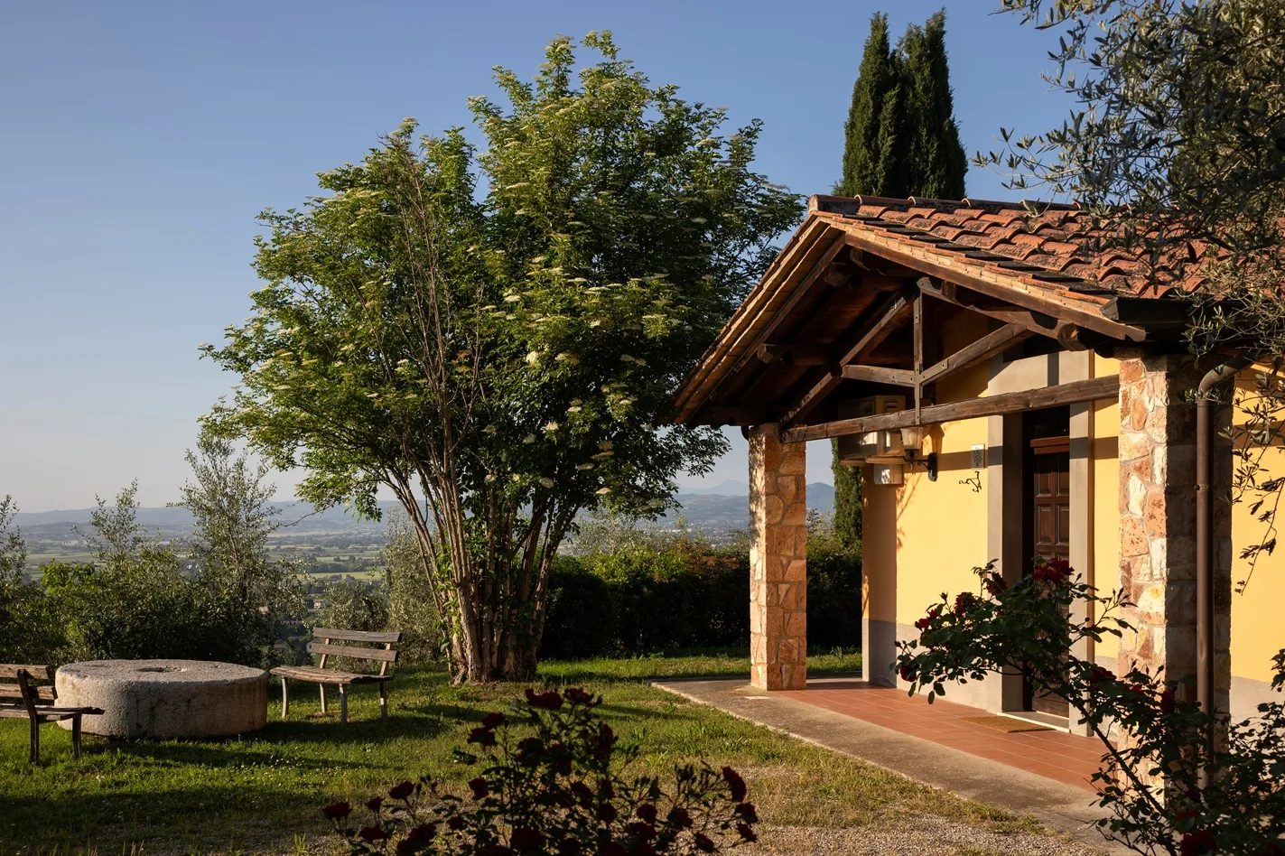 Ingresso di casa rustica in pietra con portico, giardino, panchine e vista sulla valle