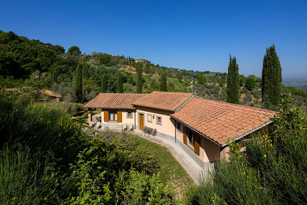 Casa colonica con tetto in cotto immersa tra cipressi, uliveti e colline verdi